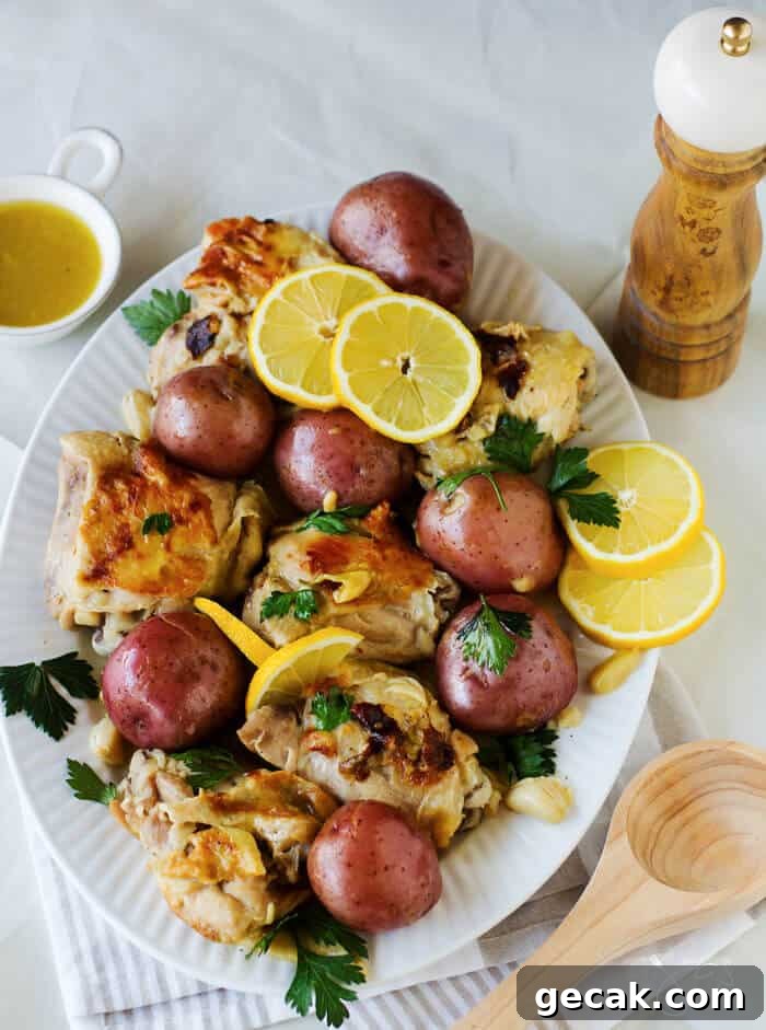 An oval plate with chicken, potatoes, and lemons sitting on a white table cloth