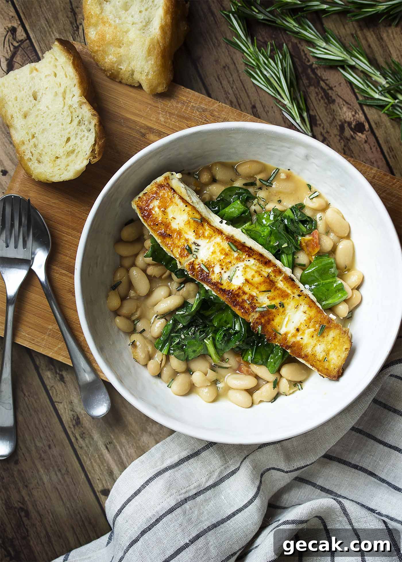 Top view of a table set with a dinner bowl of white beans, sauteed spinach, and pan seared halibut.