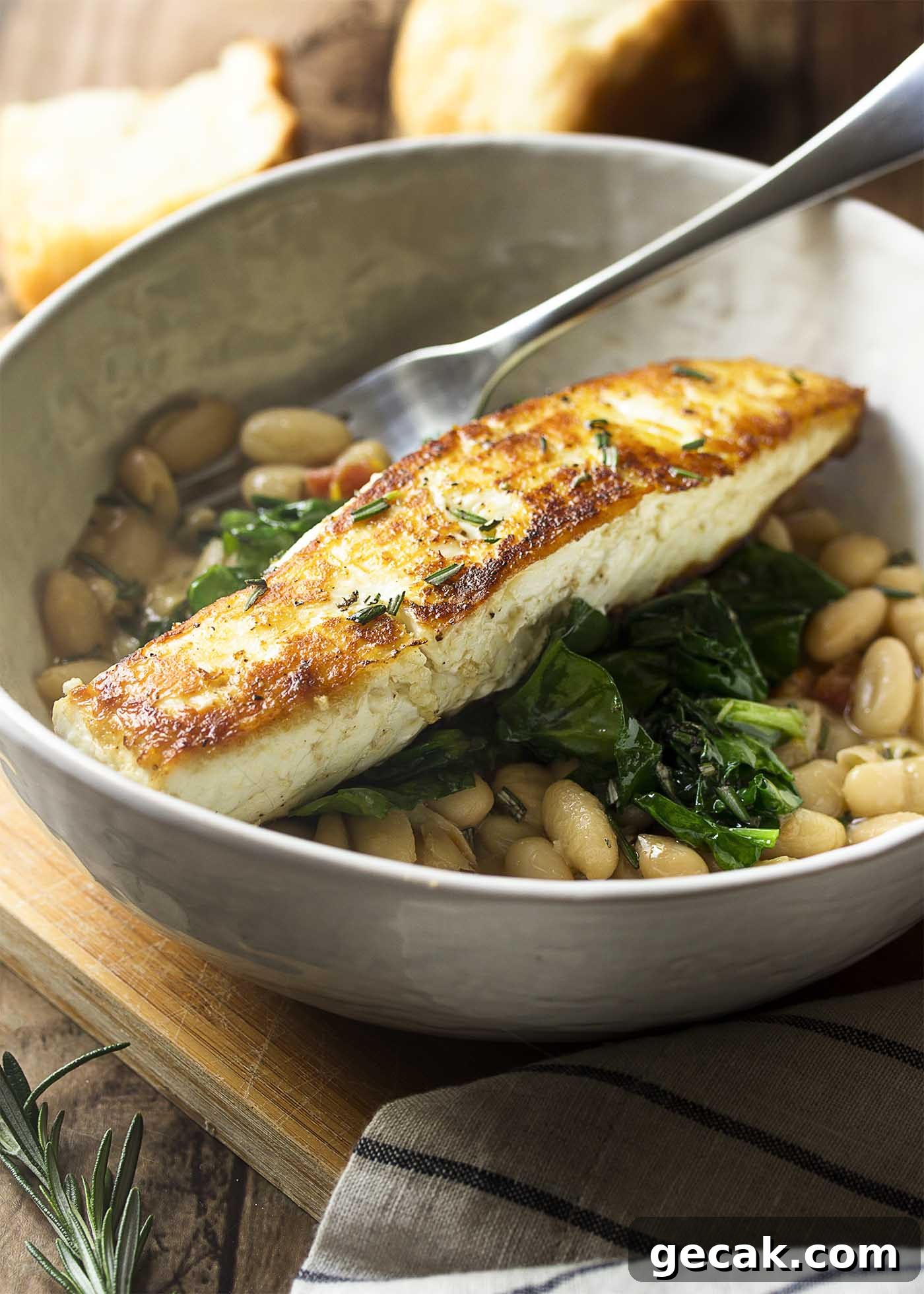 Large dinner bowl of white beans topped by sauteed spinach and a piece of golden brown fish.