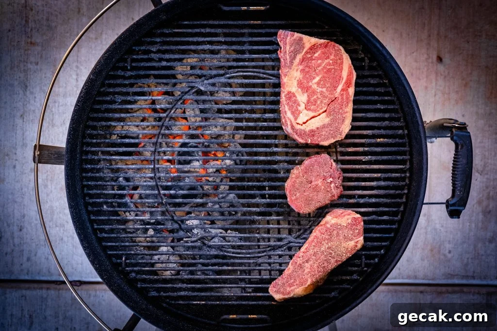 Three steaks over indirect heat on a charcoal grill.