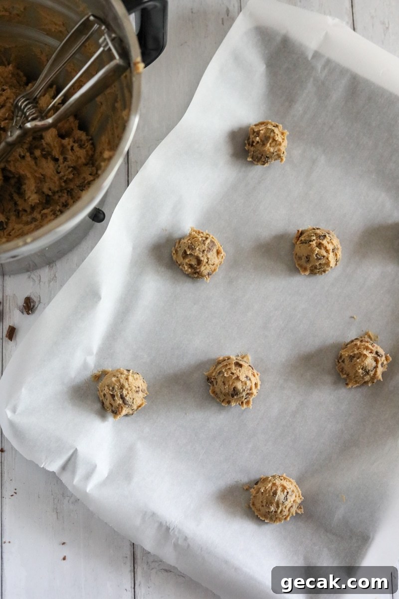 chocolate chip cookie dough balls on a sheet pan with a bowl of cookie dough off to the side