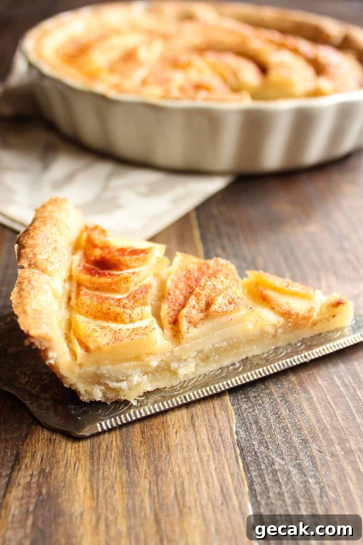 A slice of my apple tart with almond paste filling on a silver pie server.