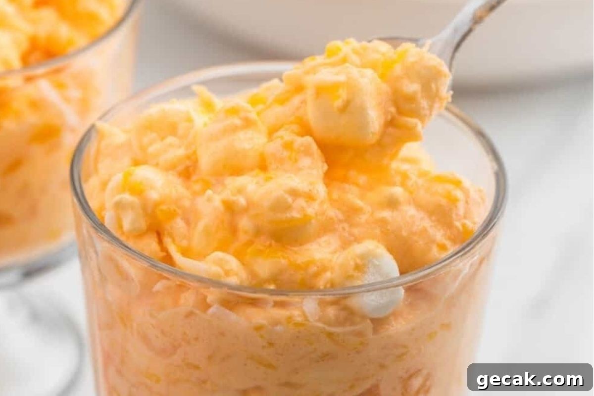 A spoonful of orange jello salad in a glass.