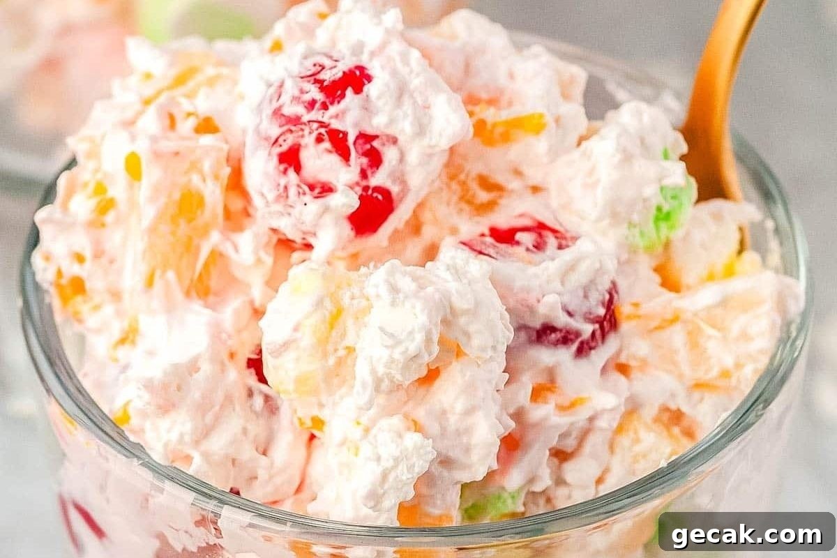 Fruit and jello salads in a glass bowl with a spoon.