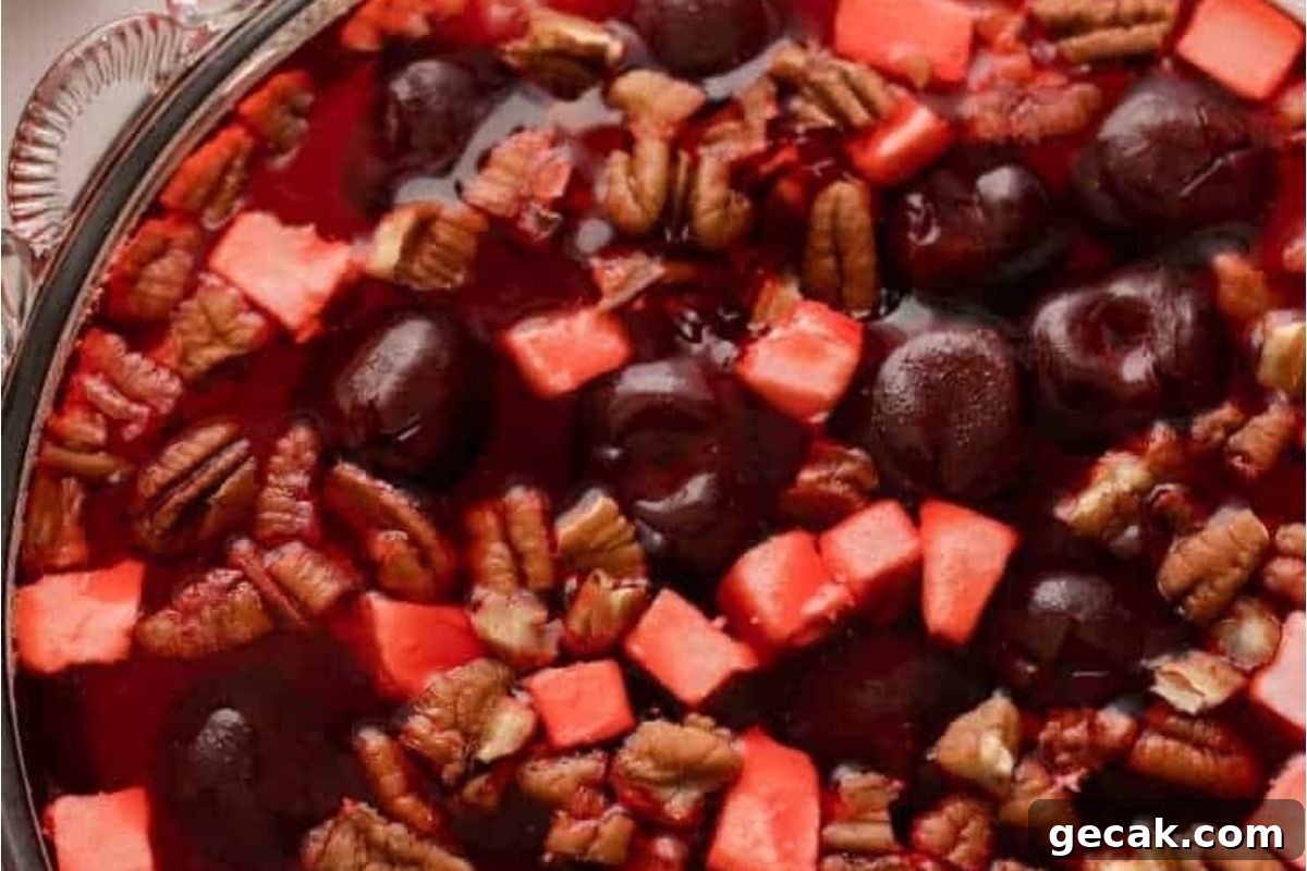 A glass bowl filled with jello salads, cherries, and pecans.