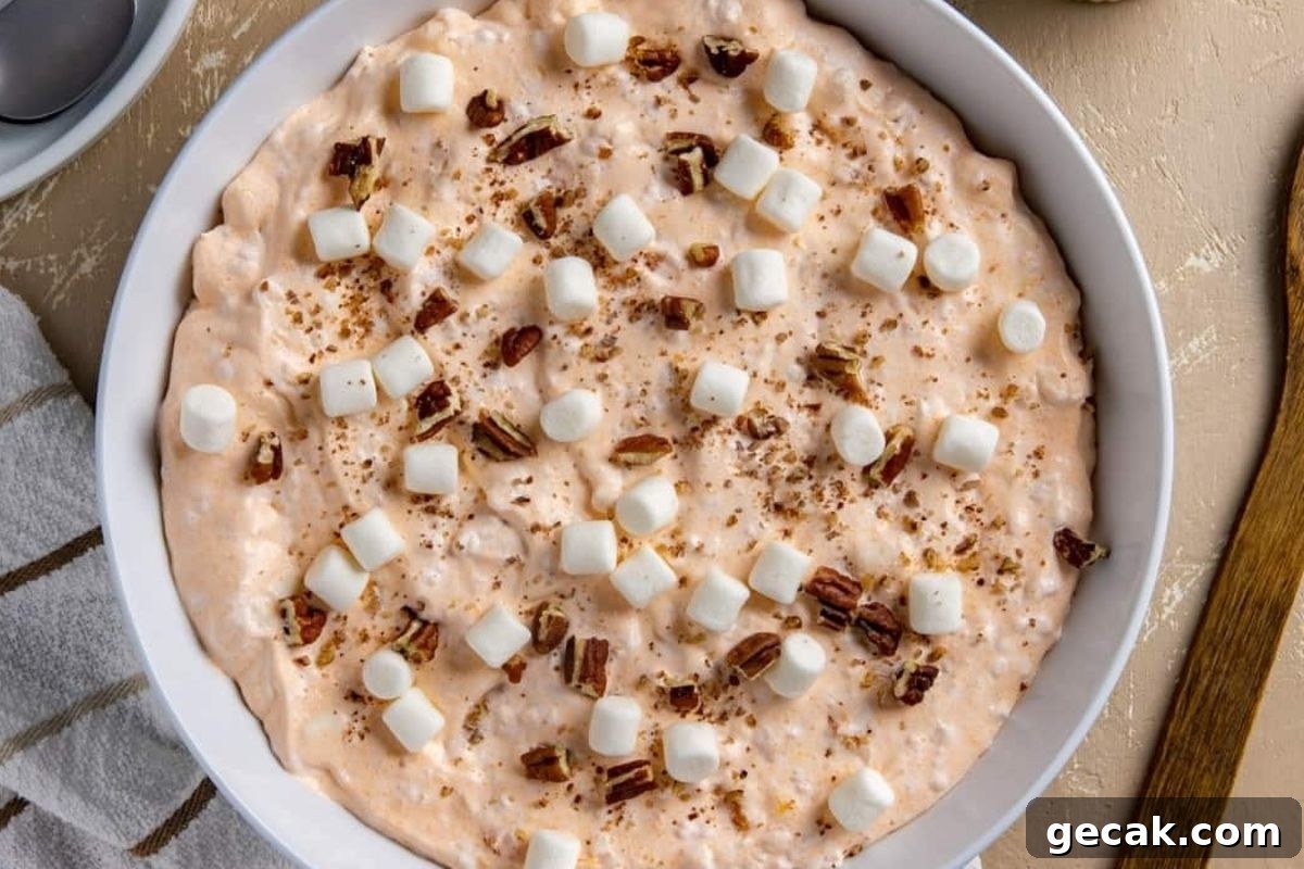 A white bowl with marshmallows, pecans, and jello salads in it.