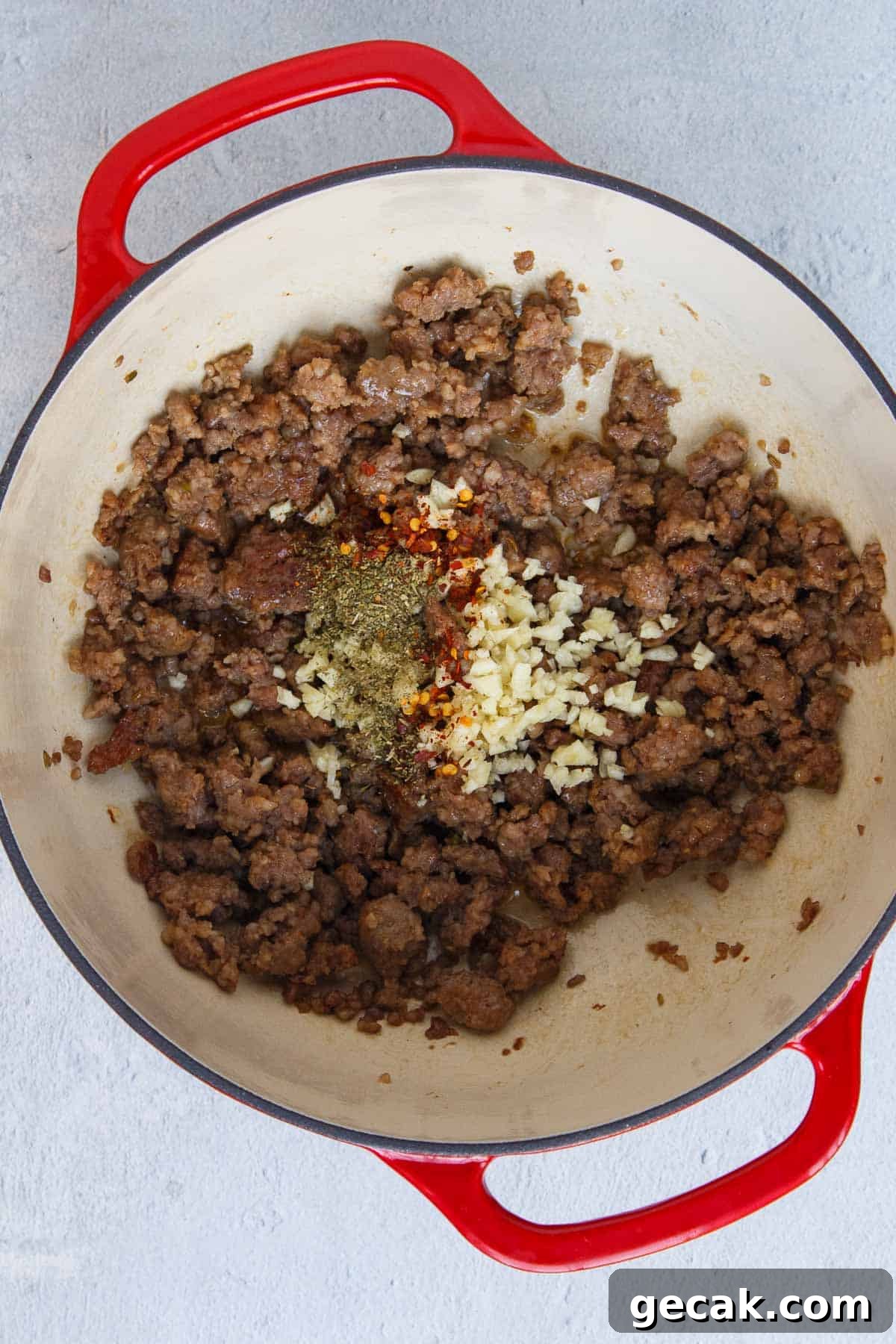 Garlic, Italian seasoning, and red pepper flakes added to cooked Italian sausage in a large pot