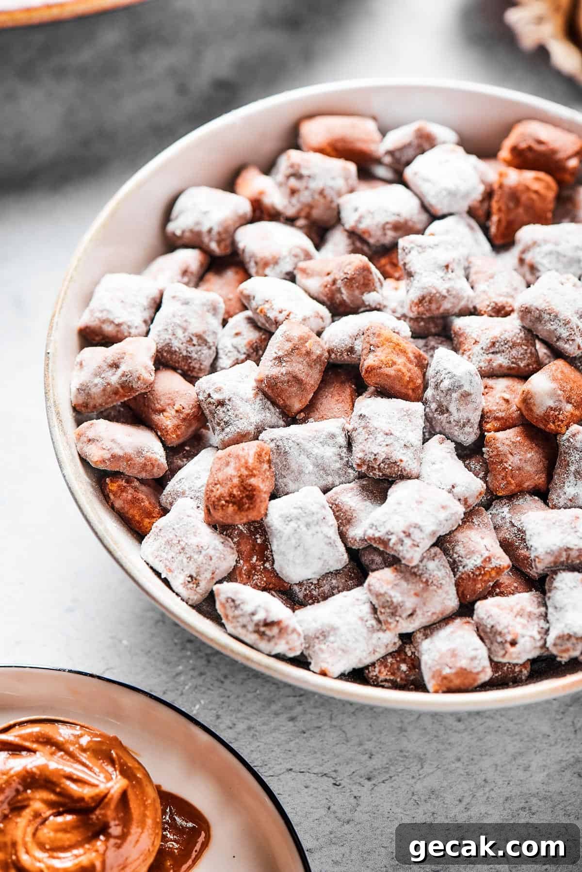 Chocolate Peanut Butter Muddy Buddies Snack Mix Recipe 8 Close-up shot of puppy chow in a white bowl, to show the texture. Some pieces are fully coated in powdered sugar, while others are not.
