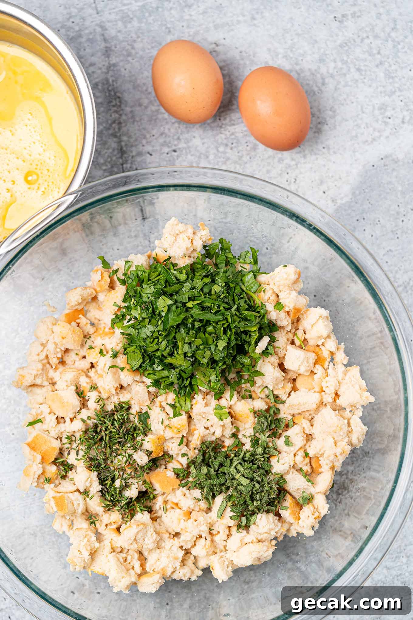 Classic Old-Fashioned Bread Stuffing Recipe for Thanksgiving 4 Preparing bread stuffing, one mixing bowl with moistened bread cubes, fresh thyme, parsley, and sage, beaten eggs in a separate bowl to the side.