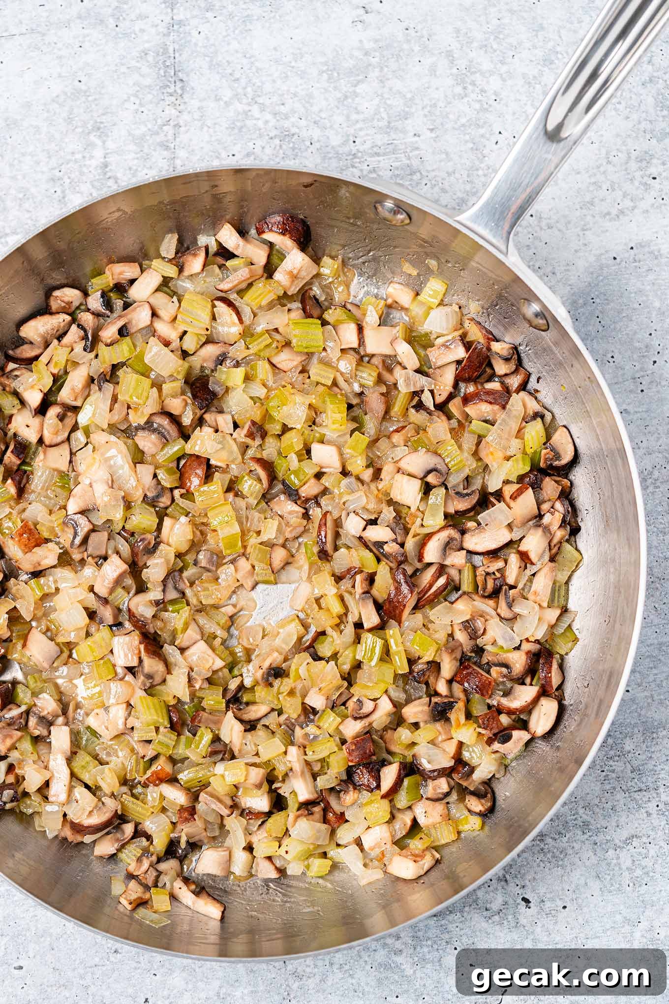 Classic Old-Fashioned Bread Stuffing Recipe for Thanksgiving 5 A frying pan filled with chopped onion, celery, and mushrooms sautéed in butter, ready to be added to homemade bread stuffing.