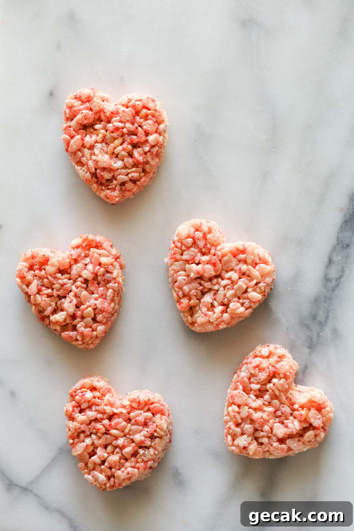 Strawberry Rice Krispie Treats Recipe – Fresh Fruity Snack 9 Overhead shot of five heart shaped Strawberry Rice Krispie Treats on a marble background.