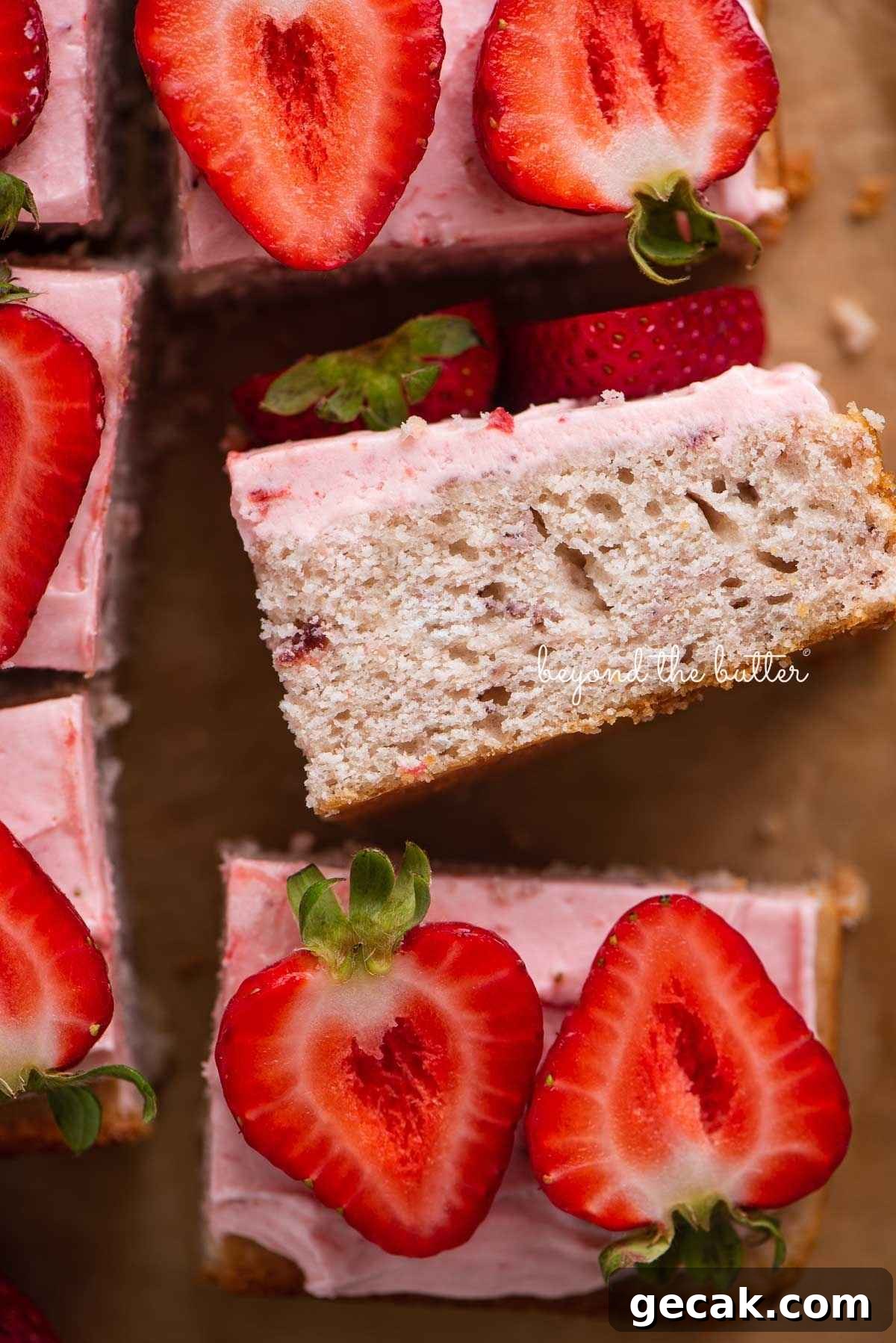 Slices of mini strawberry sheet cake topped with strawberry buttercream frosting and fresh strawberries with one slice on its side.