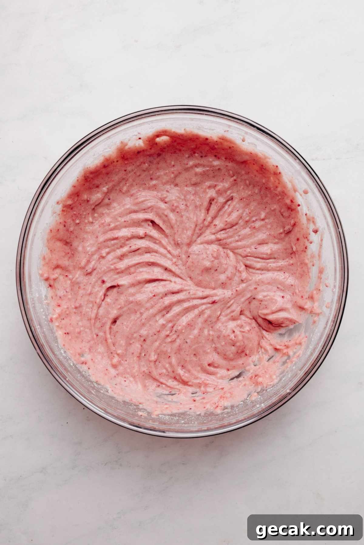 Strawberry cake batter in a large glass mixing bowl on a white and grey textured background.