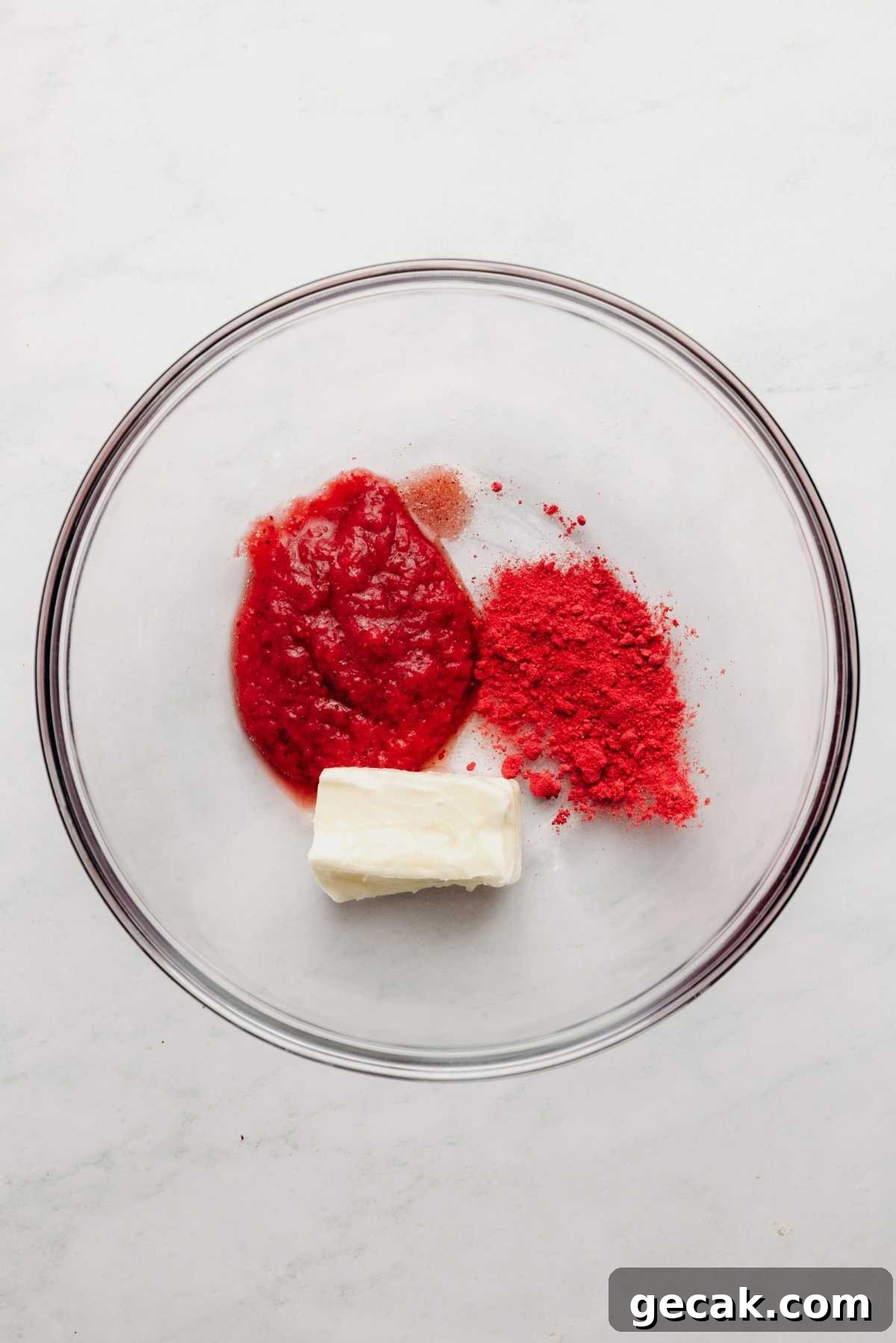 Strawberry puree, freeze dried strawberry powder, butter, and salt in large glass mixing bowl on a white and grey textured background.