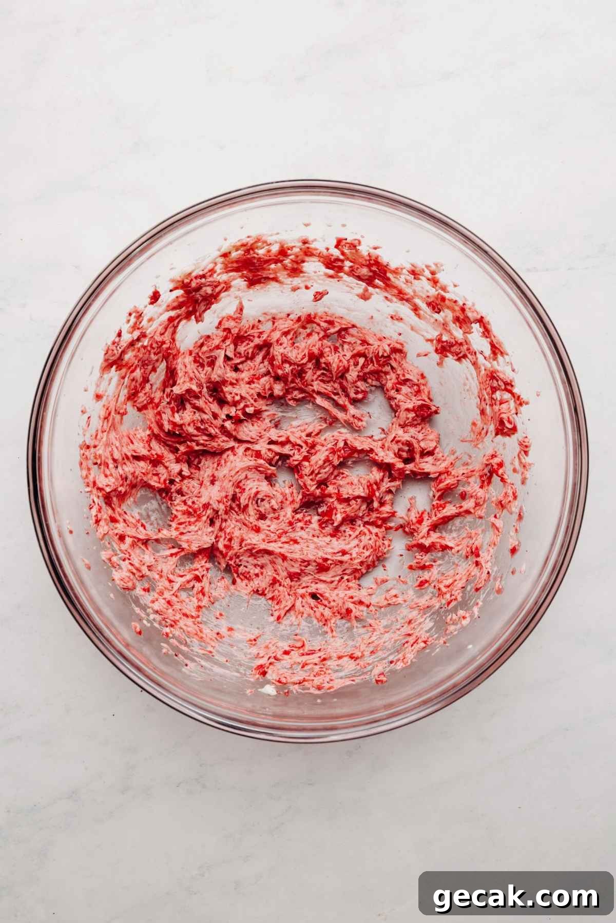 Strawberry puree, freeze dried strawberry powder, butter, and salt blended together in a large glass mixing bowl on a white and grey textured background.