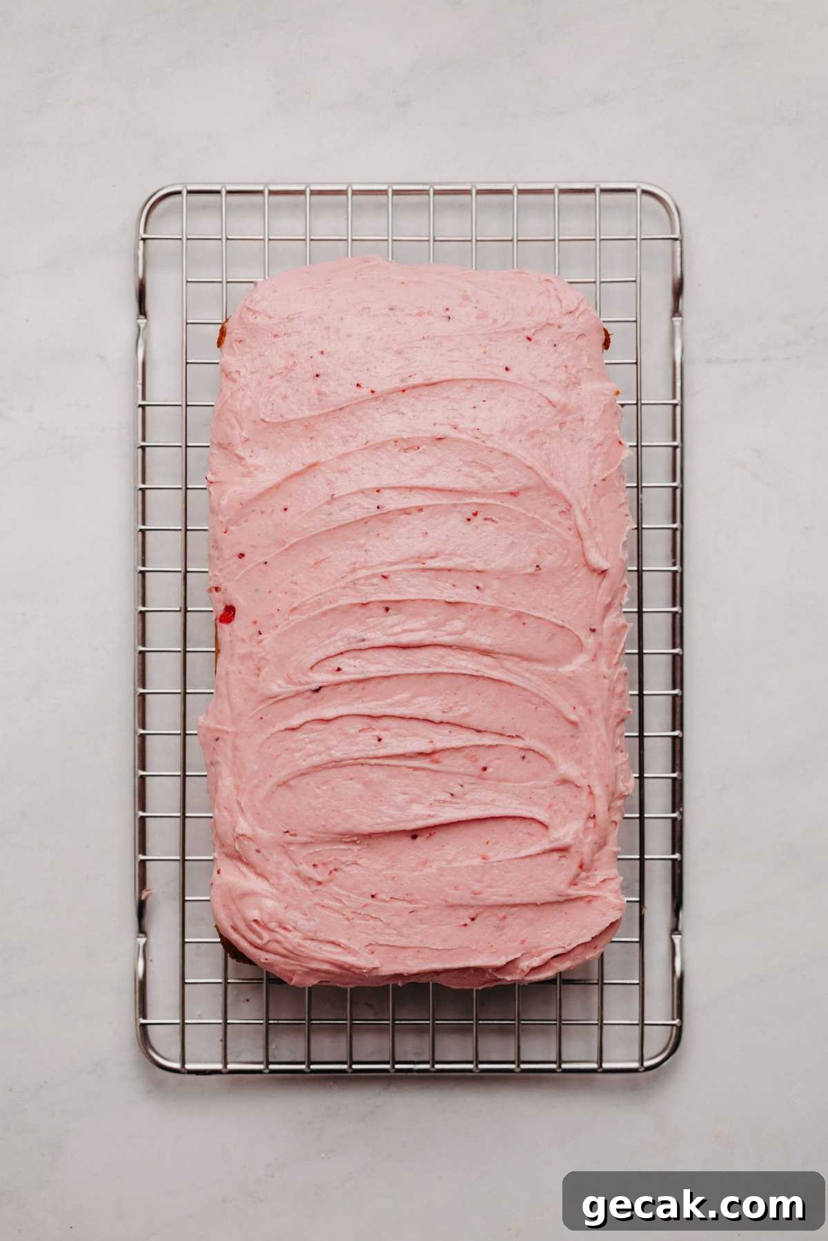 Mini strawberry sheet cake frosted with strawberry buttercream frosting on a cooling rack.