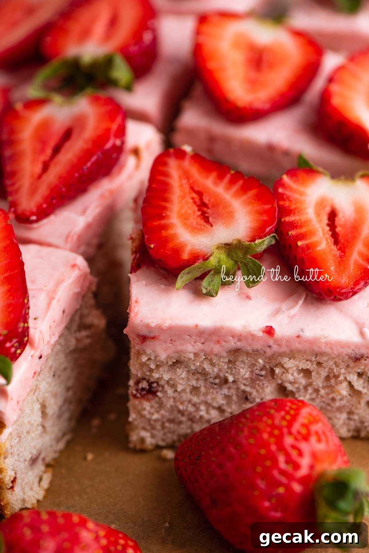 Slices of mini strawberry sheet cake topped with strawberry buttercream frosting and fresh strawberries with one slice on its side.