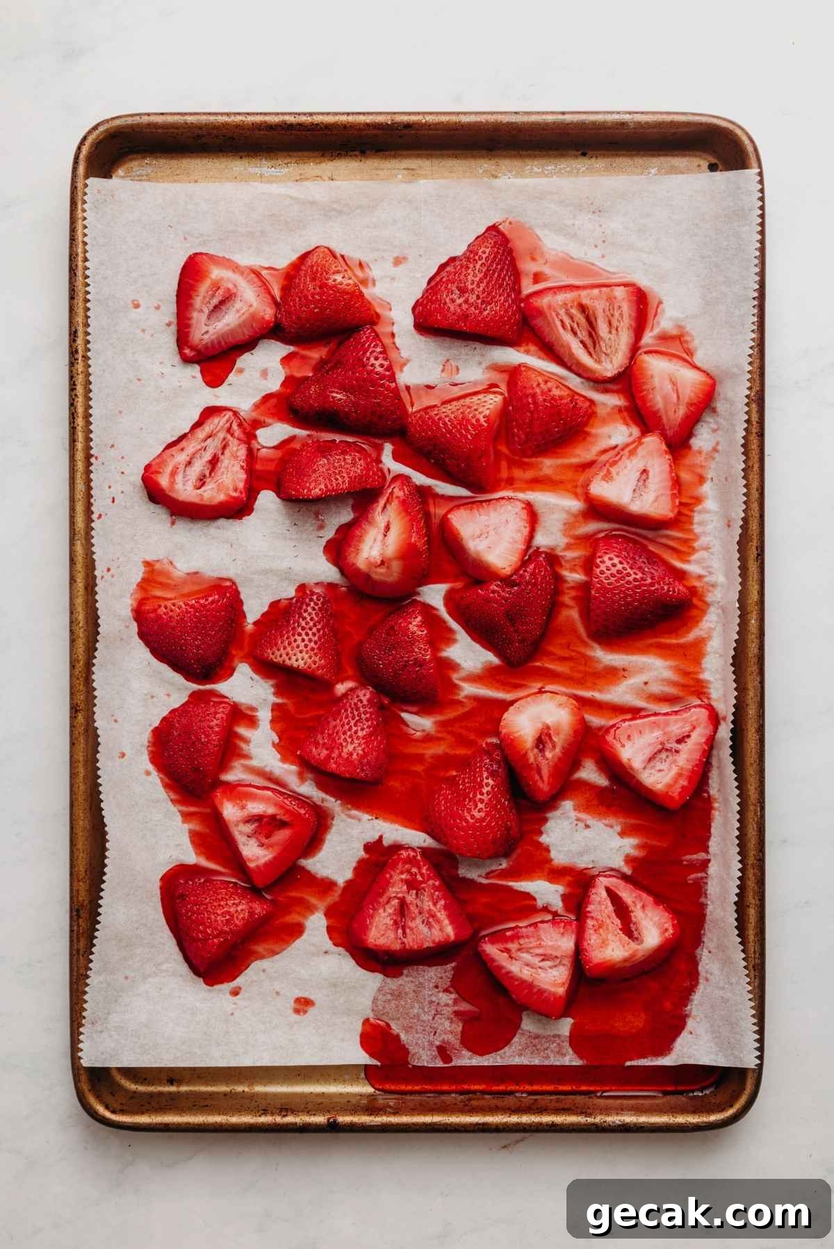 Roasted strawberries with the juices on a parchment paper lined baking sheet on a white and grey textured background.