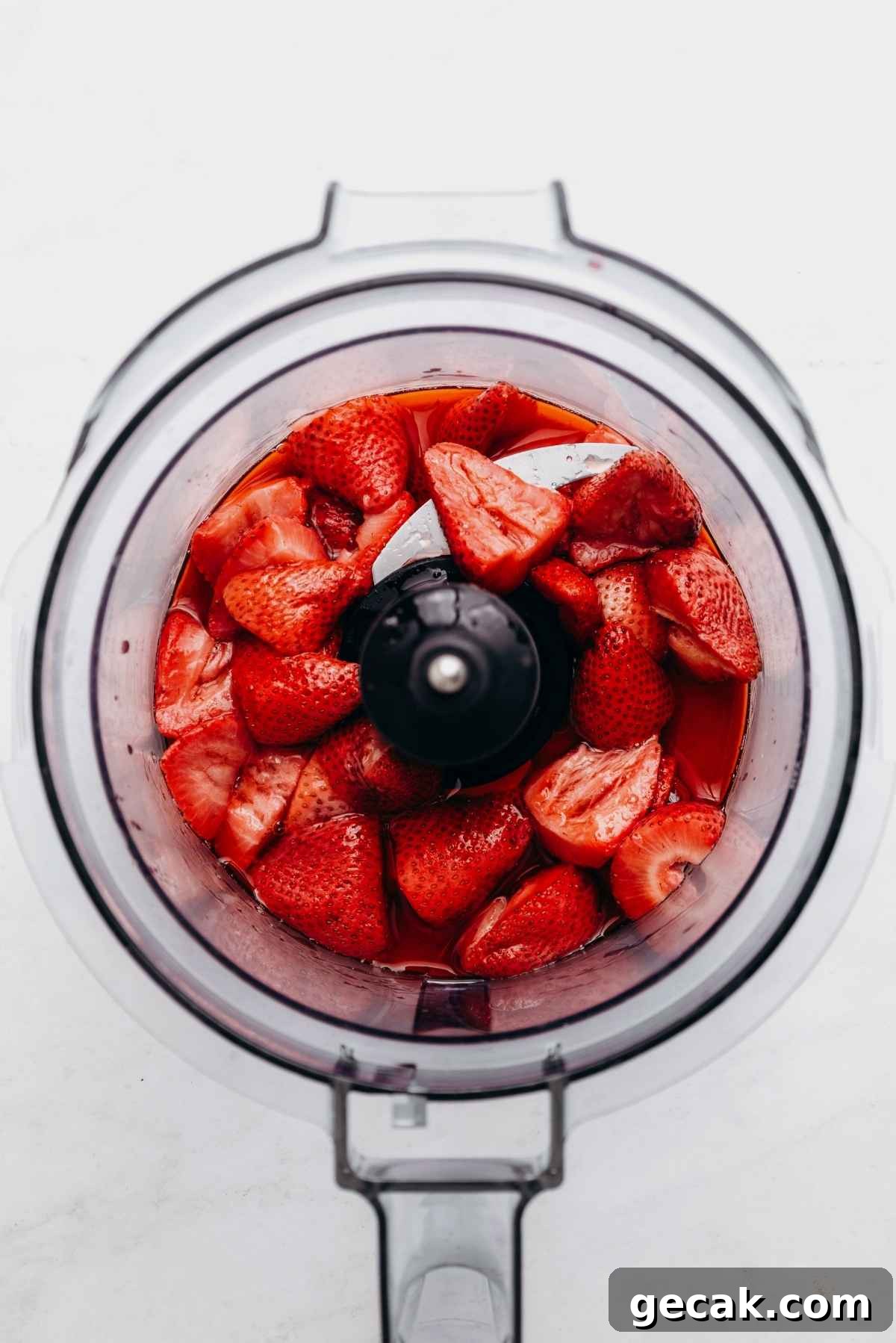 Roasted strawberries in a food processor on a white and grey textured background.
