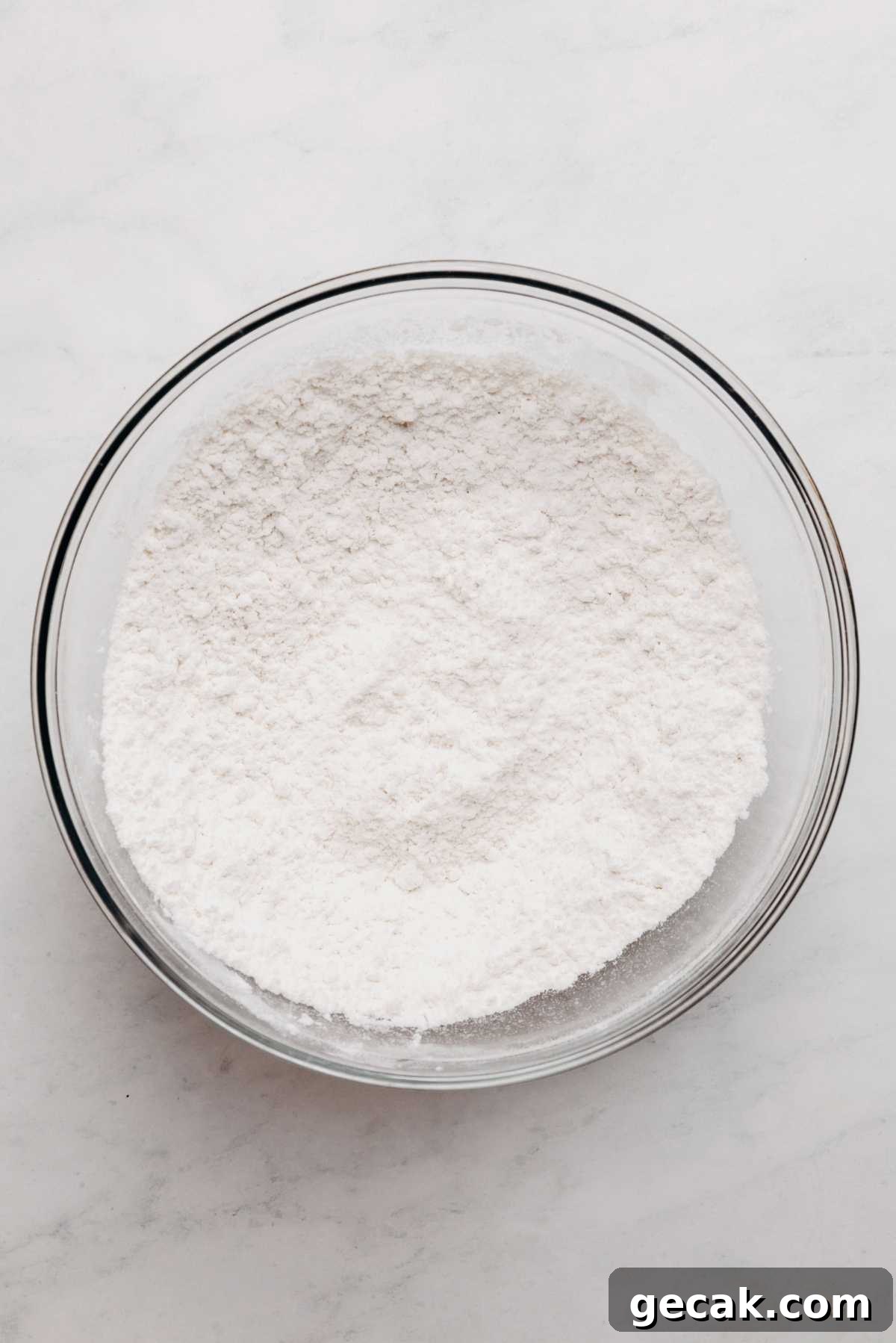 Whisked cake flour, baking powder, and salt in large glass mixing bowl on a white and grey textured background.