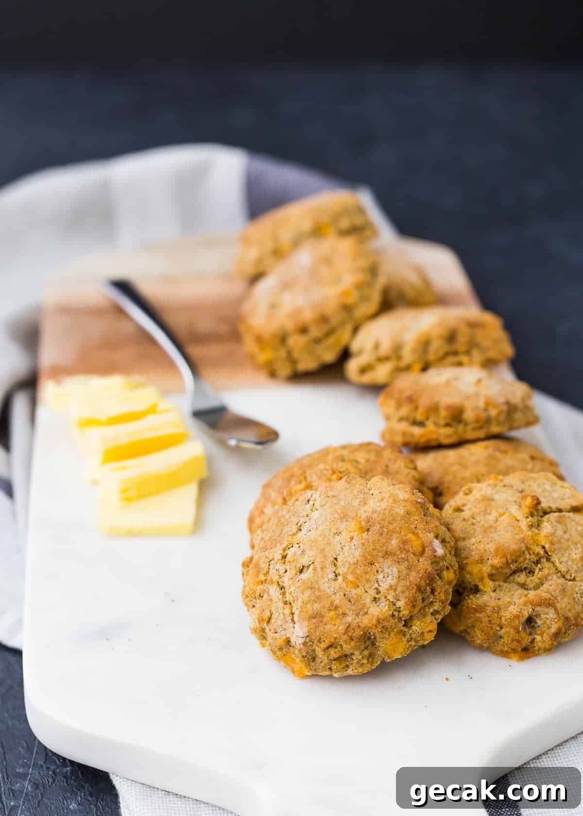 Several biscuits stacked on a white cutting board, with pats of butter and a spreader.