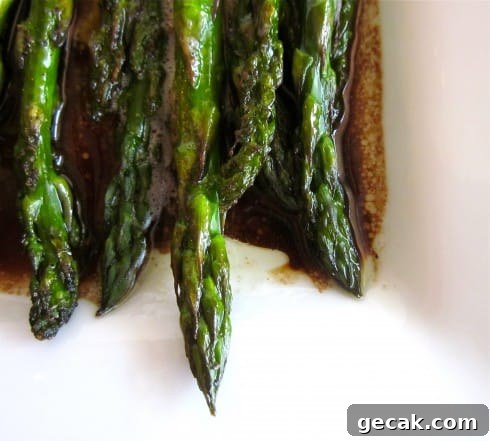 close-up of ends of oven roasted asparagus on white plate with balsamic glaze.