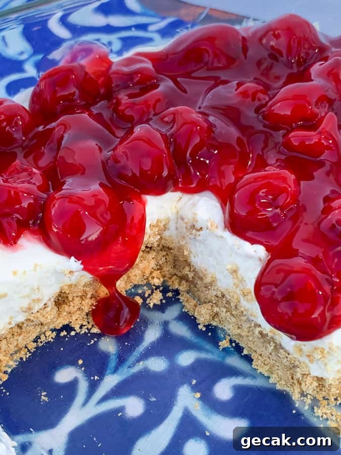 Cherry pie filling poured overtop of delight dessert in 9 inch square pan on blue napkin