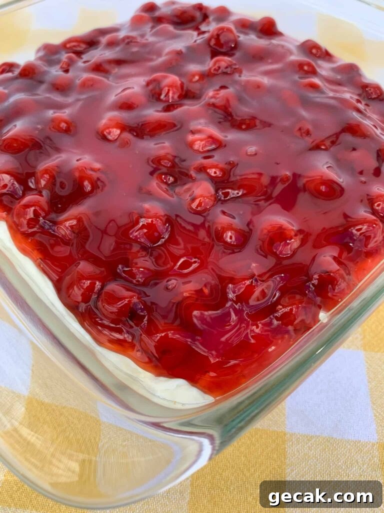 Cherry pie filling poured over whipping cream and cream cheese mixture on a graham cracker crust