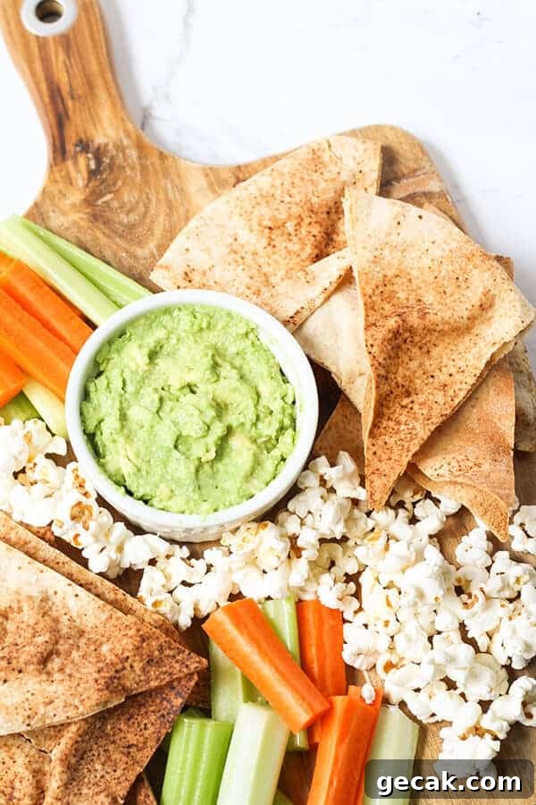 Top view of pita chips surrounded by veggies, popcorn and a green dip