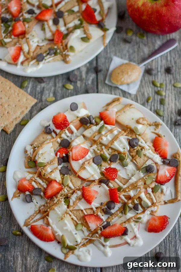 Top view of apples, strawberries, graham crackers, pepitas, chocolate chips on a white plate - after school snacks