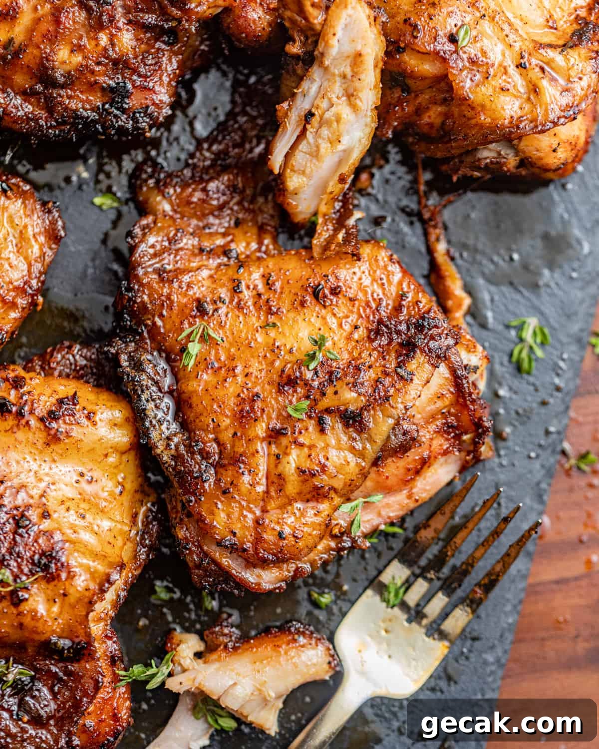 smoked chicken thighs on a plate with a fork and fresh herbs.