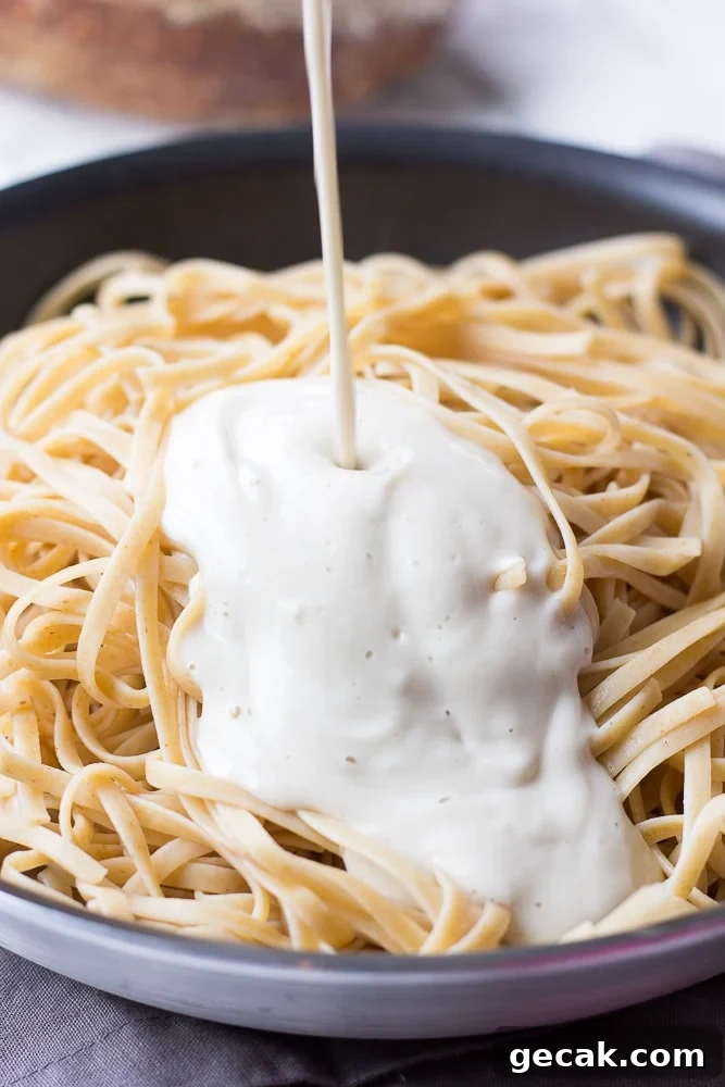 vegan alfredo sauce being poured in a pot of fettucine noodles
