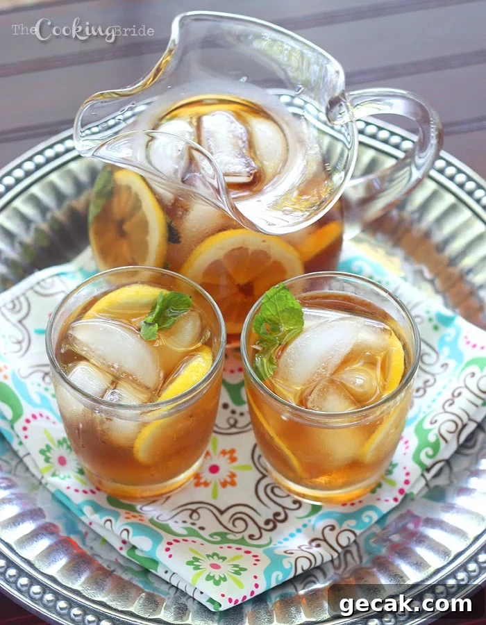 a glass pitcher of sweet tea with lemon and two serving glasses on a pewter tray with a multicolored napkin