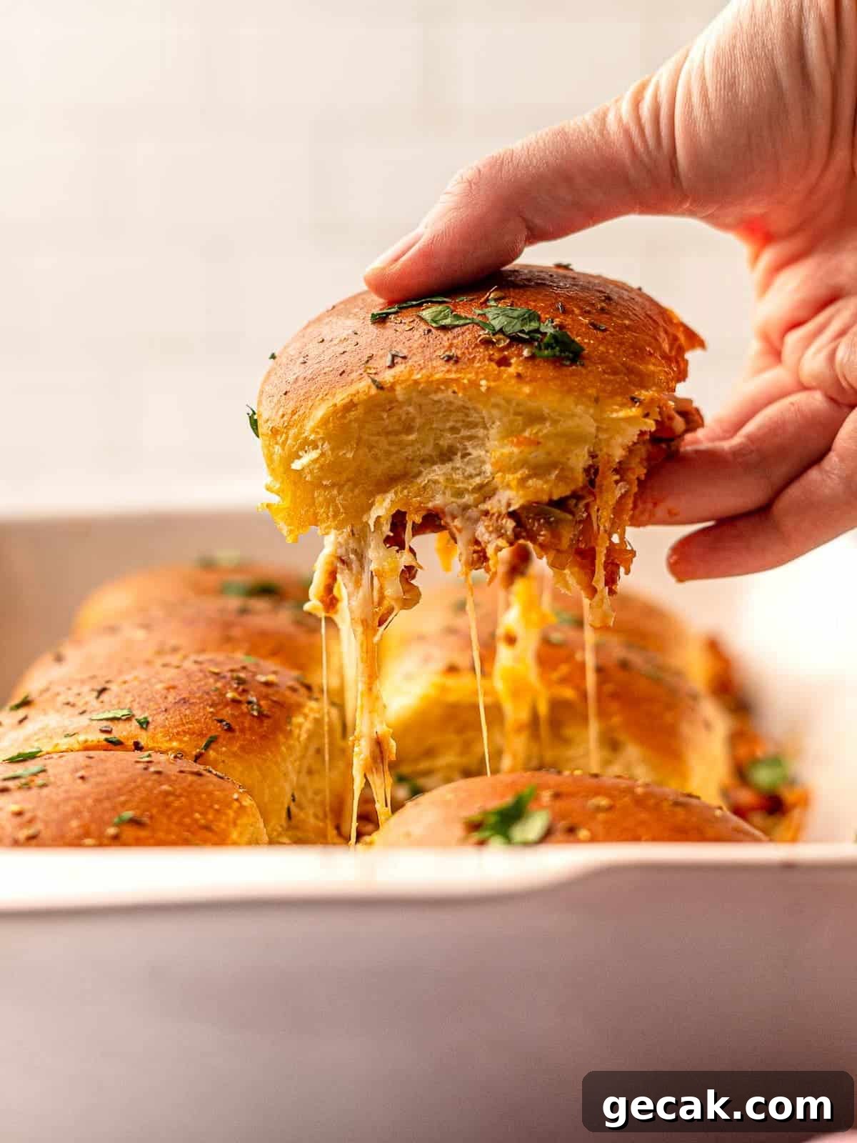 A slider being lifted out of a dish with melty cheese.