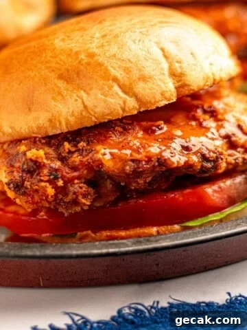 Close up view of a crispy buffalo chicken sandwich on a bun with lettuce and tomato.