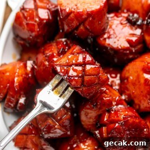 A fork holds a chunk of kielbasa in a bowl of other pieces.