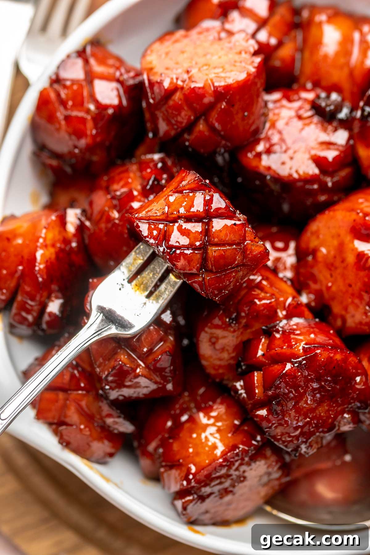 A fork holds a chunk of kielbasa in a bowl of other pieces.