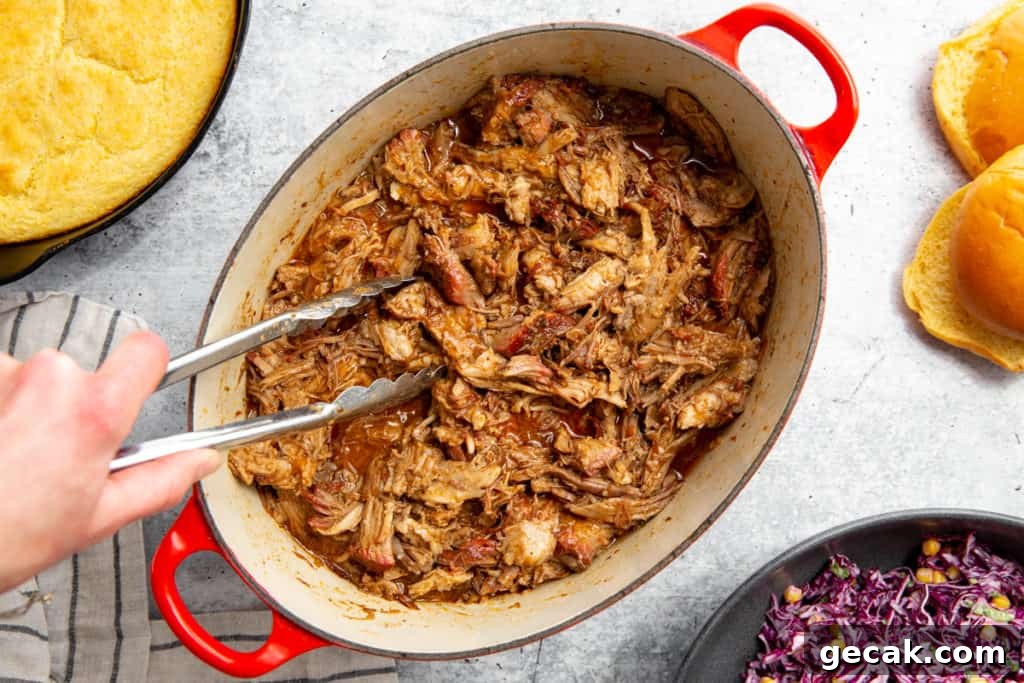 A hand grabbing smoked pulled pork from a pot using tongs.