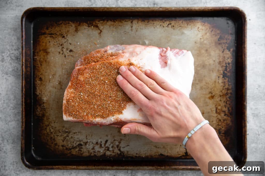 Process shot showing a hand rubbing a spice rub onto a pork butt for the Traeger pulled pork recipe.