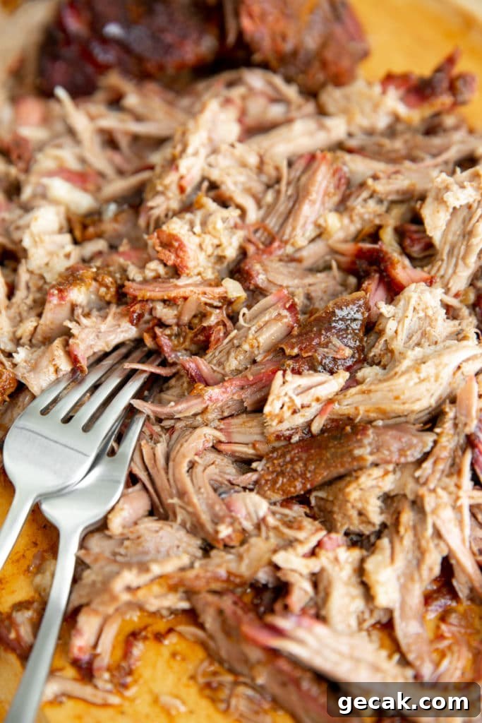 Close up of shredded smoked pork on a cutting board with two forks.