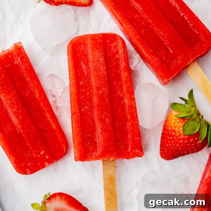 three strawberry popsicles on top of ice cubes with halved strawberries, viewed from above.