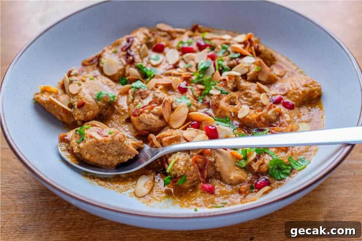 Top 10 Must-Try Recipes from 2020 for Home Cooks 6 A bowl of Mughlai Chicken Curry garnished with Almonds, cilantro and pomegranate seeds with a spoon on the side.