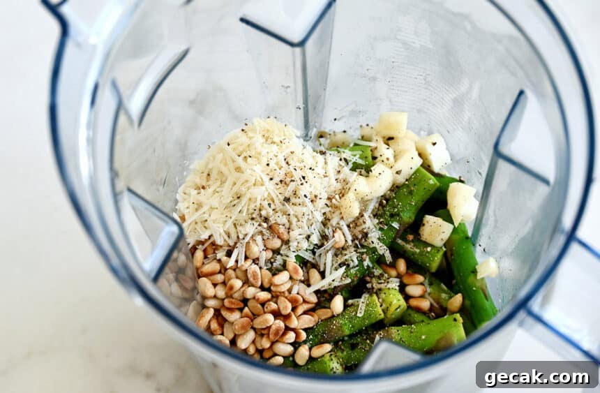 Creamy Asparagus Pesto Pasta with Parmesan 4 A top-down view of a blender containing toasted pine nuts, shredded Parmesan cheese, garlic cloves, salt and pepper