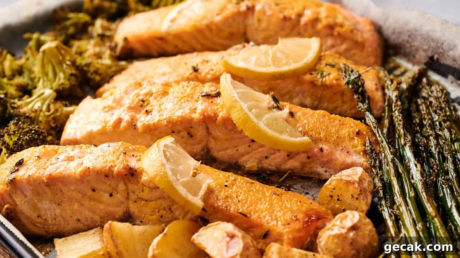 Baked salmon fillets garnished with lemon slices, served with roasted broccoli, asparagus, potatoes, and garlic cloves on a sheet pan.