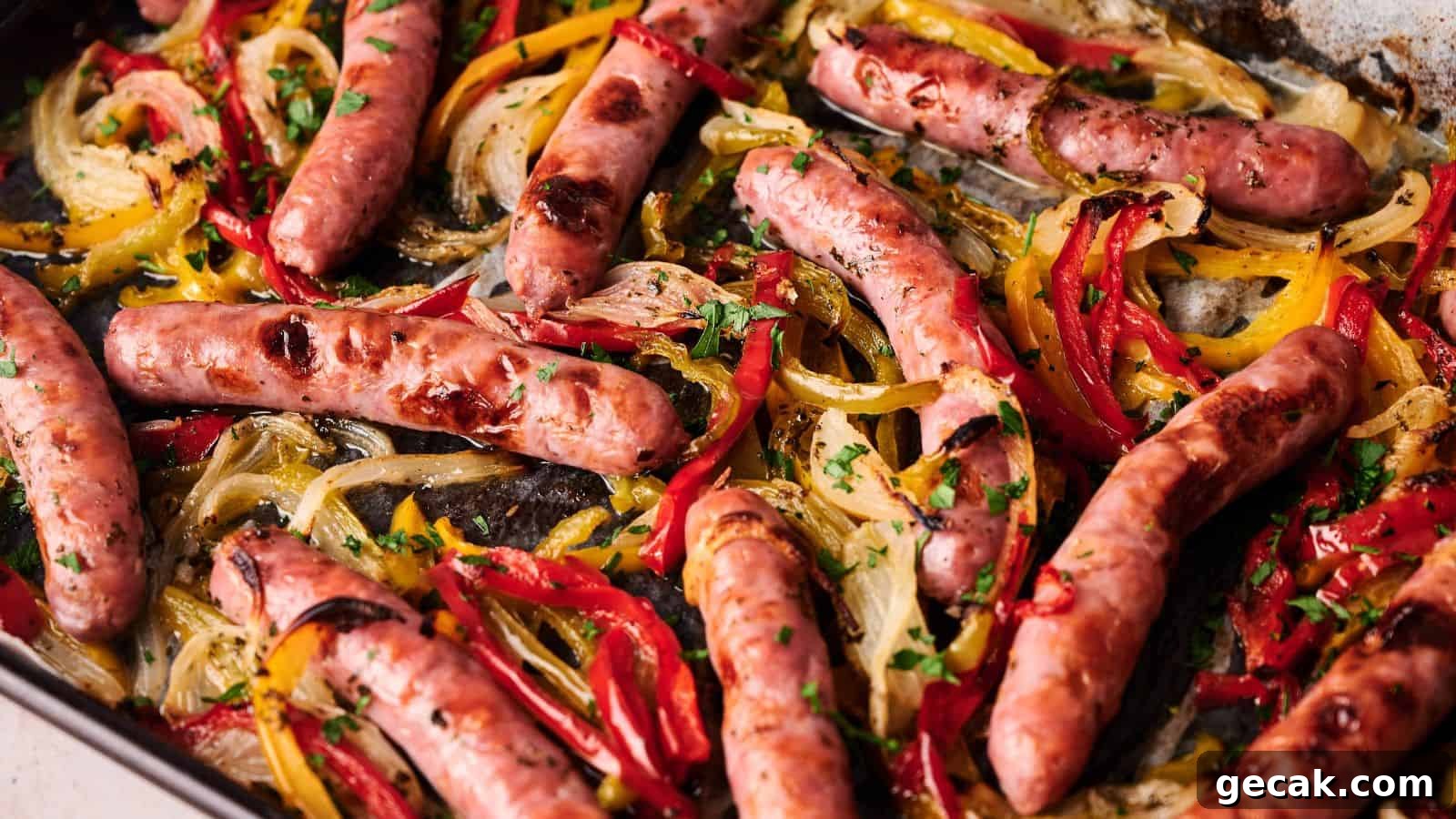 Sheet pan with roasted sausages, sliced red and yellow bell peppers, and onions, garnished with chopped parsley.