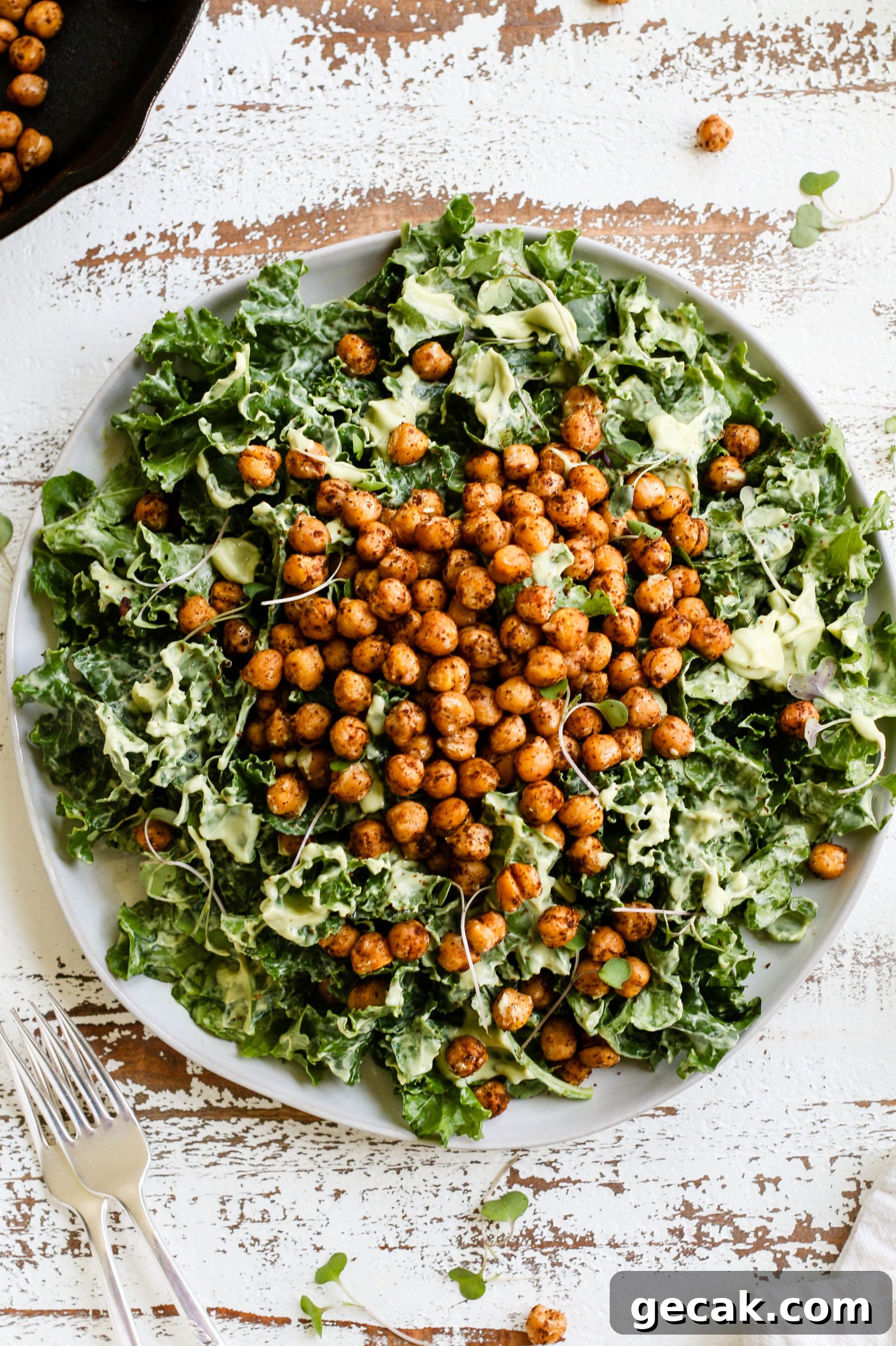 Kale Caesar Salad with Avocado Dressing served on a plate on a white distressed wooden board with two forks and skillet of chickpeas in the corner by Flora & Vino 