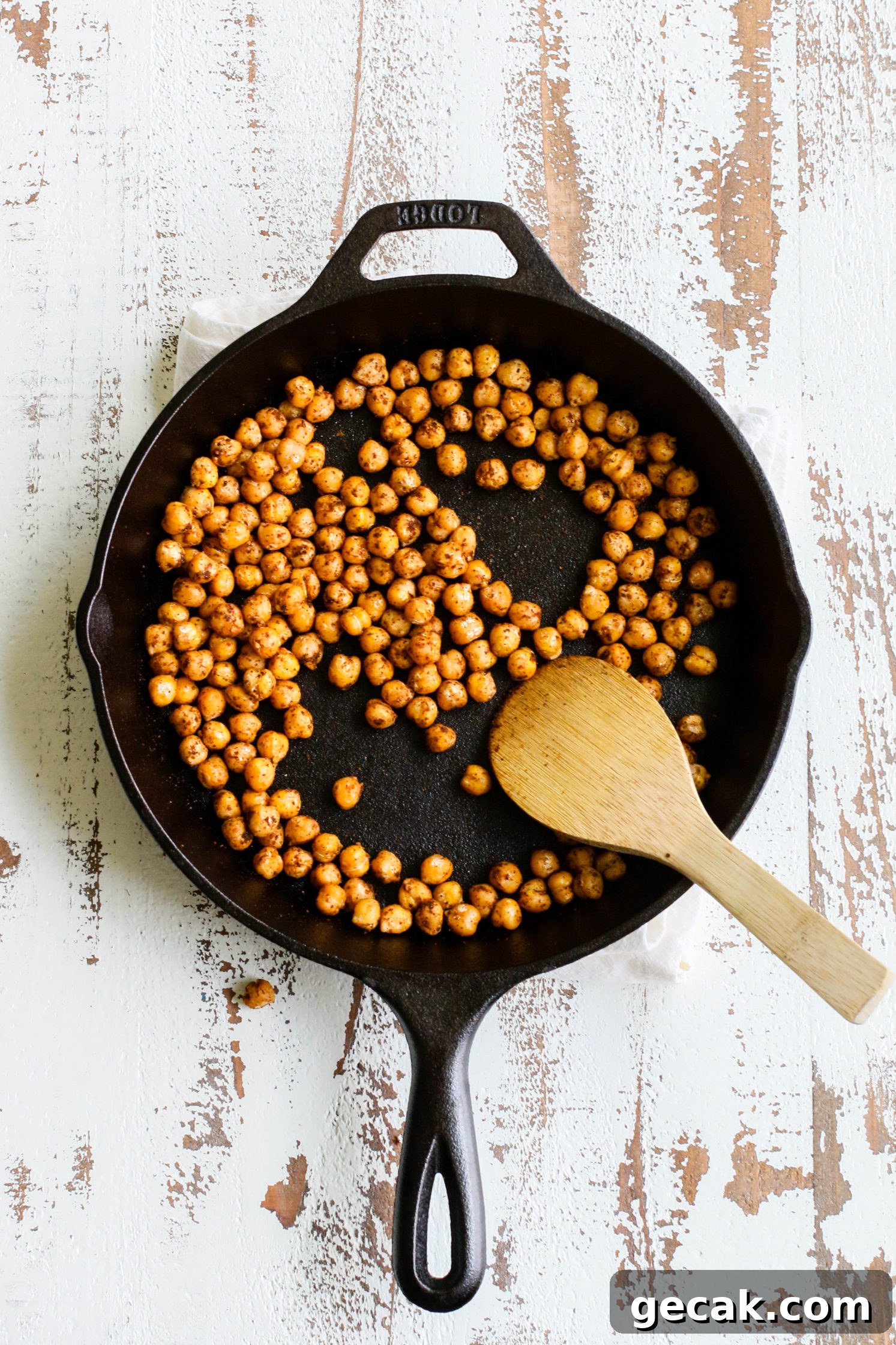 crispy Tandoori Masala seasoned chickpeas in cast iron skillet with wooden spoon on distressed white board by Flora & Vino 