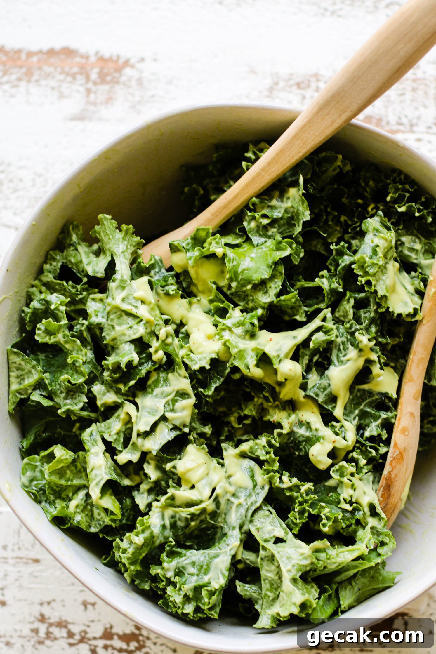 kale leaves in white bowl topped with avocado cream dressing with two wooden salad tongs by Flora & Vino 