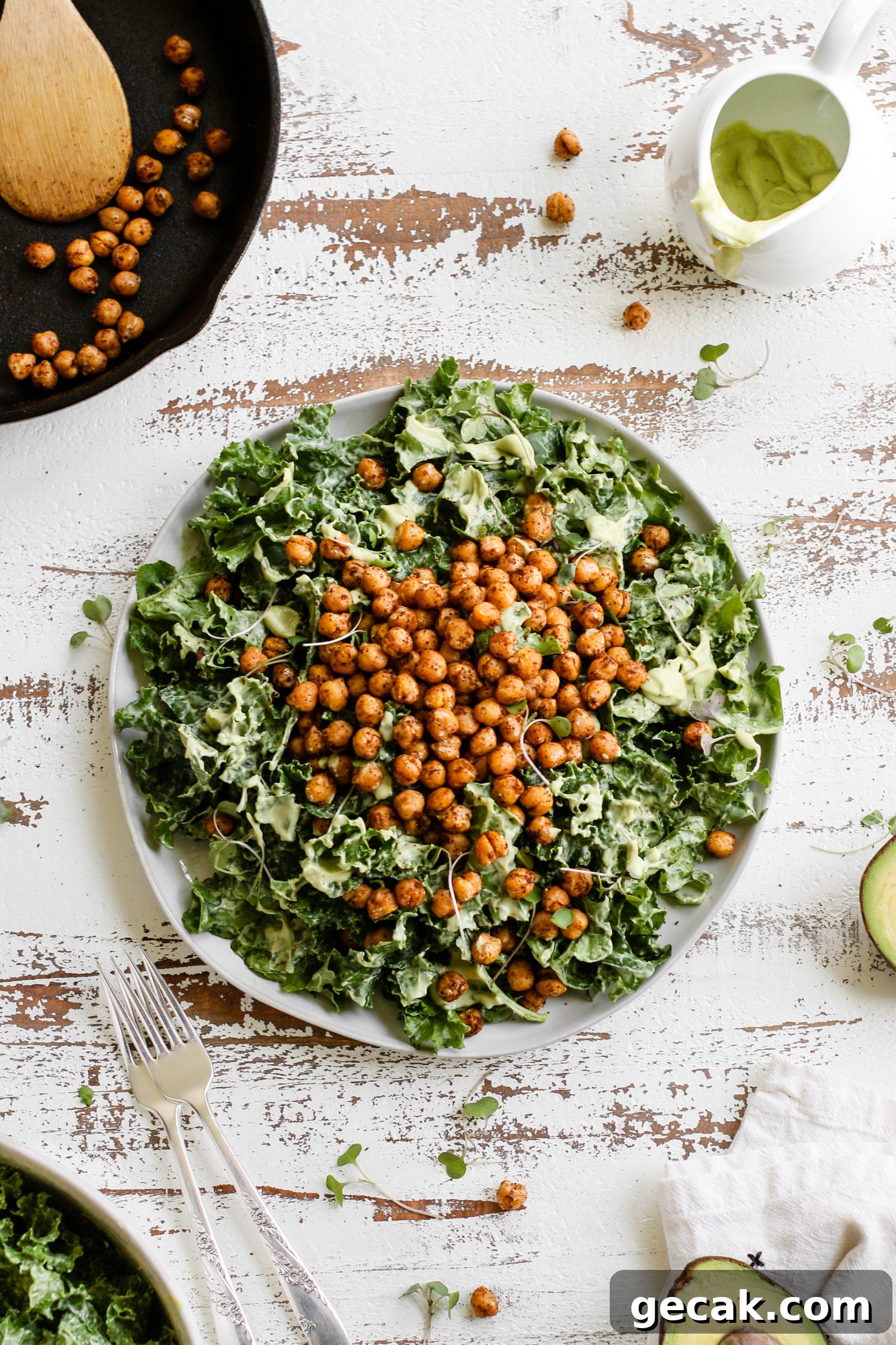 Kale Caesar Salad with Avocado Dressing served on a plate on a white distressed wooden board with two forks and skillet of chickpeas in the corner by Flora & Vino 