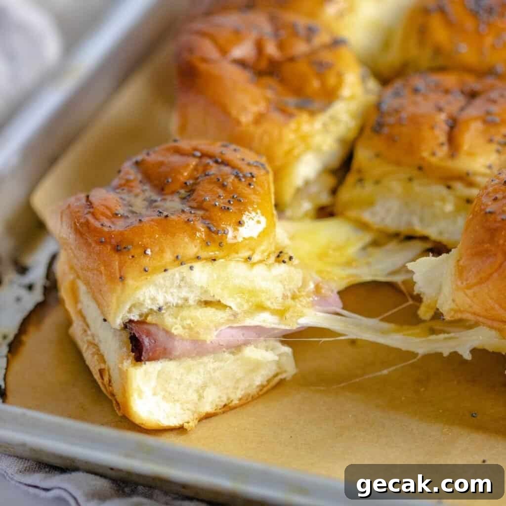 Baked ham and cheese sliders on a sheet pan being pulled apart.